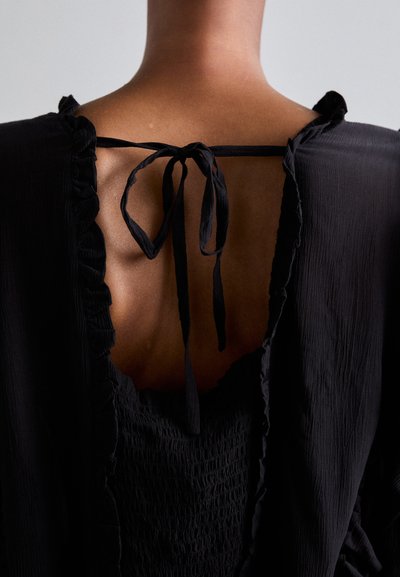 Black dress with a ruffled neckline and back tie detail. The fabric appears lightweight and textured, with a smocked design at the bodice.