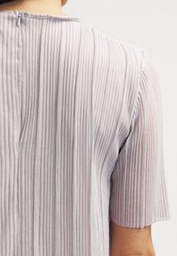 Haut plissé violet clair à manches courtes, doté de rayures texturées verticales et d'une petite fermeture éclair dans le dos.