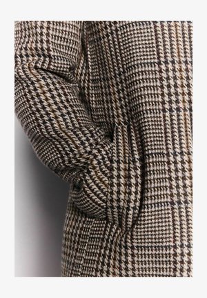Barna és bézs hounds-tooth mintázatú kabát, texturált anyagból, laza fazonnal és oldalsó zsebbel az ujjon.