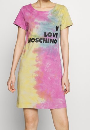 Kobieta w sukience typu shift z krótkim rękawem w stylu tie-dye w kolorach różowym, żółtym i niebieskim z napisem „LOVE MOSCHINO” i czarnym sercem nadrukowanym na piersi.