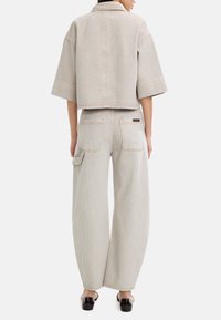 Przycięta jasnoszara dżinsowa kurtka z szerokimi rękawami, połączona z luźnymi jasnoszarymi spodniami z dwoma tylnymi kieszeniami i jedną kieszenią boczną.