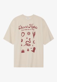 Beige oversized t-shirt met een rode grafische print van sterren, cactussen, een slang en cowboylaarzen. Ronde halslijn en korte mouwen.
