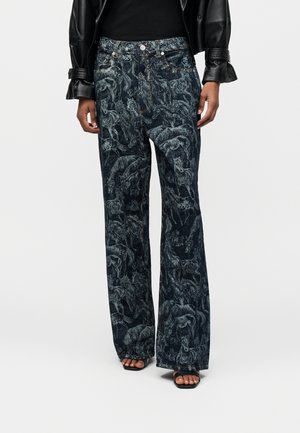 Ciemnoniebieskie szerokie jeansy z detalicznymi wzorami koni, noszone z czarnym topem, skórzaną kurtką i czarnymi sandałami na otwartym palcu.