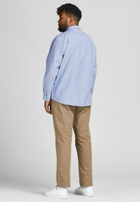 Camisa de botones azul claro, pantalones caqui y zapatillas blancas. La camisa tiene un corte relajado y mangas largas con puños.