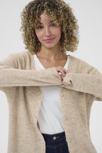 Beige texturerad cardigan med långa ärmar och knapplåsning, lager på en vit skjorta, med ribbad stickad mönster och tumhål.