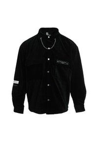 Camisa de pana negra con diseño de botones, grandes bolsillos en el pecho, un detalle de cadena en el cuello y un acabado texturizado.