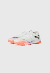 Weiße Sportschuhe mit pink- und blaufarbigen Farbverlauf, Obermaterial aus Mesh, strukturierte Sohle und kontrastierendes schwarzes Logo. Für Rasenplätze designt.