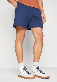 Shorts de sport en coton bleu marine avec une coupe décontractée et des poches latérales, associés à des baskets blanches montantes et des chaussettes de longueur mi-mollet.