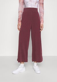 Bordeaux wijde broek met een elastische tailleband, gemaakt van zachte stof, gecombineerd met witte sneakers en enkelsokken.