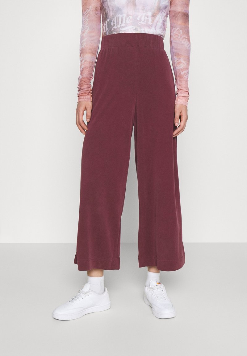 Bordeaux wijde broek met een elastische tailleband, gemaakt van zachte stof, gecombineerd met witte sneakers en enkelsokken.