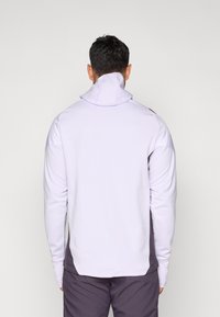 Lys lilla sportsgenser med høy krage, lange ermer og kontrasterende mørkegrå detaljer på sidene og nederst på kanten. Glatt tekstur.