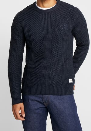 Granatowy sweter z dzianiny z teksturowanymi wzorami, okrągłym dekoltem, ściągaczami przy mankietach i u dołu, z małą metką marki po lewej stronie.