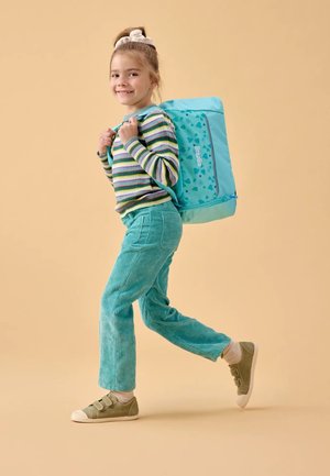 Teal backpack with heart pattern; girl wearing striped long-sleeve top, turquoise corduroy pants, and green sneakers, smiling.