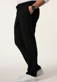 Mustat urheiluhousut, joissa on joustava vyötärö, sivutaskut ja teksturoitu kangas, yhdistettynä valkoisiin urheilukenkiin.