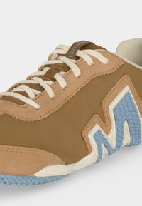 Baskets couleur beige avec lacets crème, motif "M" texturé bleu sur le côté et doublure intérieure crème rembourrée.