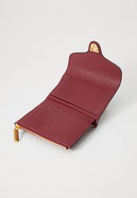 Portafoglio in pelle bordeaux con finitura testurizzata, accessori in oro, scomparti per carte, tasca con zip e design con bordo superiore curvato.