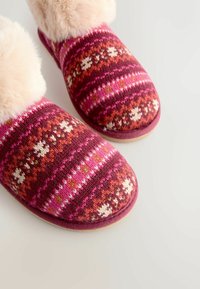 Adītas čības ar rozā un burgundijas zīmējumu, kurām ir mākslīgā kažokāda uz apmalēm. Apaļā purngalā un teksturēts auduma dizains augšdaļā.