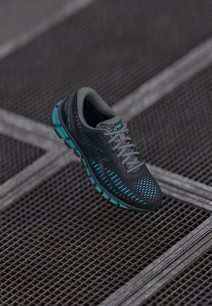 Black running shoe with turquoise accents and grey mesh upper, featuring a textured sole and a dynamic pattern of blue lines.