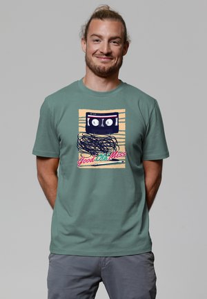 Green cotton t-shirt featuring a graphic of a cassette tape with tangled tape and the text "Good Old Mess" in vibrant colors.