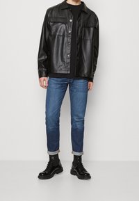 Musta keinonahkainen takki kauluksella ja kahdella etutaskulla, yhdistetty tummansinisiin farkkuihin ja mustiin nauhanilkkureihin.