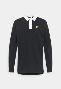 Polo de manga larga negro con cuello blanco y tapeta de botones, que presenta un pequeño logo de Nike en amarillo en el lado izquierdo del pecho.