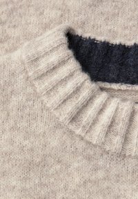 Beige gestrickter Pullover mit einem gerippten Kragen und weicher Textur. Der innere Kragen zeigt einen dunkleren Marinefarbton, der einen Kontrast bietet.