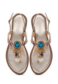 Sandalias planas en tono dorado con una correa beige, que cuentan con embellecimientos de piedras preciosas coloridas en azul, púrpura y amarillo en el separador y la parte superior.