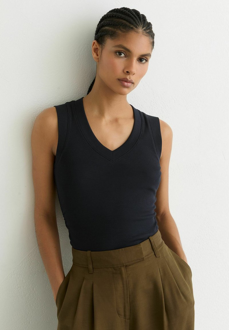 Marineblauw geribd tanktopje met V-hals, nauwsluitend silhouet en mouwloos ontwerp, gecombineerd met beige hoge taillebroeken.