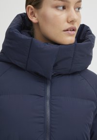 Navy puffer jacket with a high, structured collar, zipper front closure, and smooth texture. Features a lightweight design for warmth.