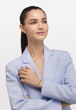 Brăță de argint pe unÎncheietura mâinii, cu un design elegant și un model texturat. Modelul poartă un sacou bleu deschis, evidențiind moda minimalistă.