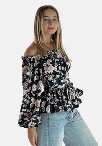 Off-the-shoulder sort bluse med blomsterprint, flæser på ærmerne, indsnævret talje og peplum nederdel. Har en snøre detaljer og lette blomster mønstre.