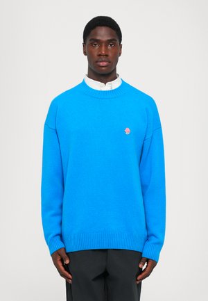 Helles blaues Strickpullover mit gerippten Bündchen und Saum, verziert mit einer kleinen pinken gestickten Blume auf der Brust. Lässige Passform.