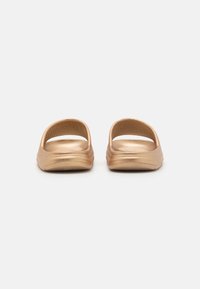 Sandale slip-on aurii cu un finisaj metalic neted, design cu degetele deschise și o talpă interioară texturată pentru aderență. Marginile rotunjite, cu profil redus.