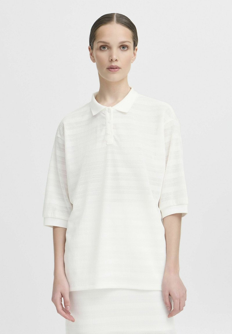 Witte polo met korte mouwen en een gestructureerd patroon, voorzien van een drieknops sluiting. Zachte stof met een lichte glans, met ribgebreide manchetten.
