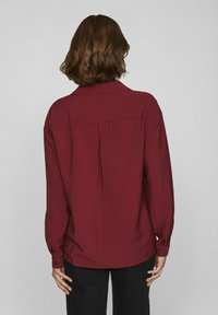 Camisa de manga larga burdeos con tejido texturizado, que presenta un cuello clásico, puños abotonados y un pliegue en la espalda para un detalle adicional.