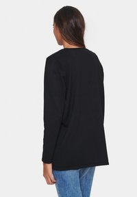 Črna majica z dolgimi rokavi, sproščenega kroja, okroglega izreza, rebraste teksture in minimalističnega dizajna; v kombinaciji z svetlo modrimi kavbojkami.