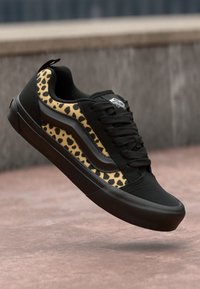 Sorte sneakers med leopardmønstrede detaljer, laget av et strukturert materiale, flate lisser og gummisåle. Diskret logo på tungen.