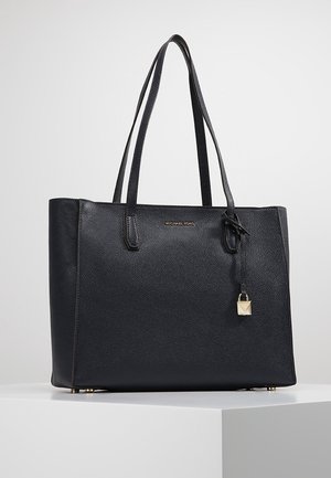 Sac fourre-tout en cuir texturé noir avec doubles anses d'épaule, plaque logo dorée, et détail de cadenas doré suspendu sur une surface blanche.