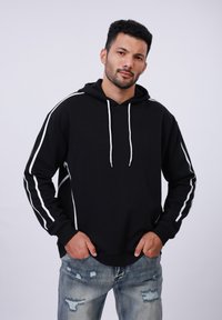 Zwarte hoodie met witte zijstrepen, gemaakt van zachte stof, met een relaxte pasvorm en een voorke pocket. Gecombineerd met versleten jeans.