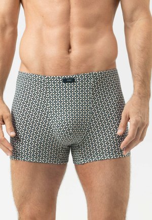Mannelijk bovenlijf met patroonboxershorts met geometrisch ontwerp, staand met ontspannen armen tegen een effen achtergrond.