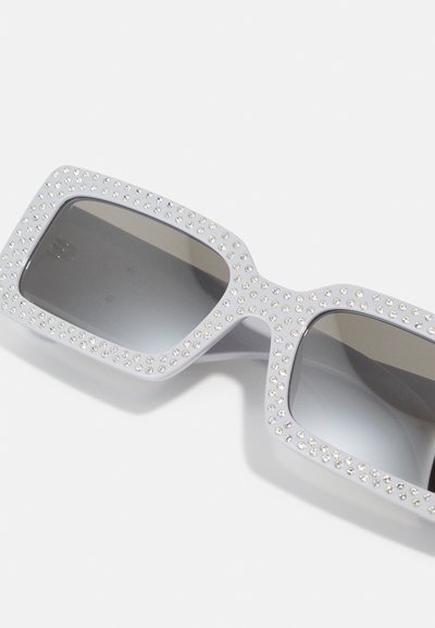 Lunettes de soleil carrées avec une monture gris clair, ornées de strass autour des bords, dotées de verres teintés foncés.