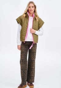Olivově zelená prošívaná vesta se světle růžovým zipem, kombinovaná s kalhotami se zvonovými nohavicemi v leopardím vzoru a hnědými platformovými botami. Měkká látka a pohodlný střih.
