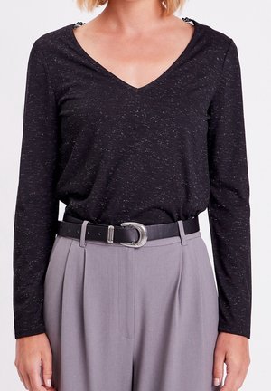 Woman wearing black long-sleeve V-neck shirt tucked into high-waisted gray pants with black belt featuring silver buckle.