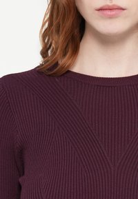 Burgundy ribbad stickad topp med diagonala texturerade mönster och rund halsringning, i ett mjukt och lättviktsmaterial.