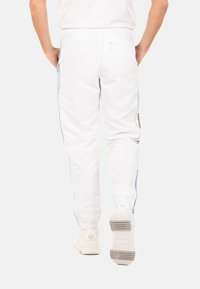 Pantalons blancs avec des panneaux latéraux bleu clair, taille élastique et poche zippée. Poignets ajustés et marquage minimal sur le côté.