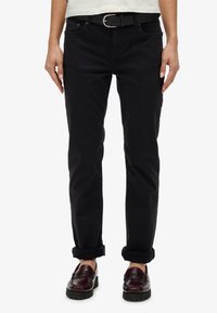 Pantalones ajustados negros de algodón, con cinco bolsillos y puños enrollados. Combinados con un cinturón negro y mocasines burdeos oscuros.