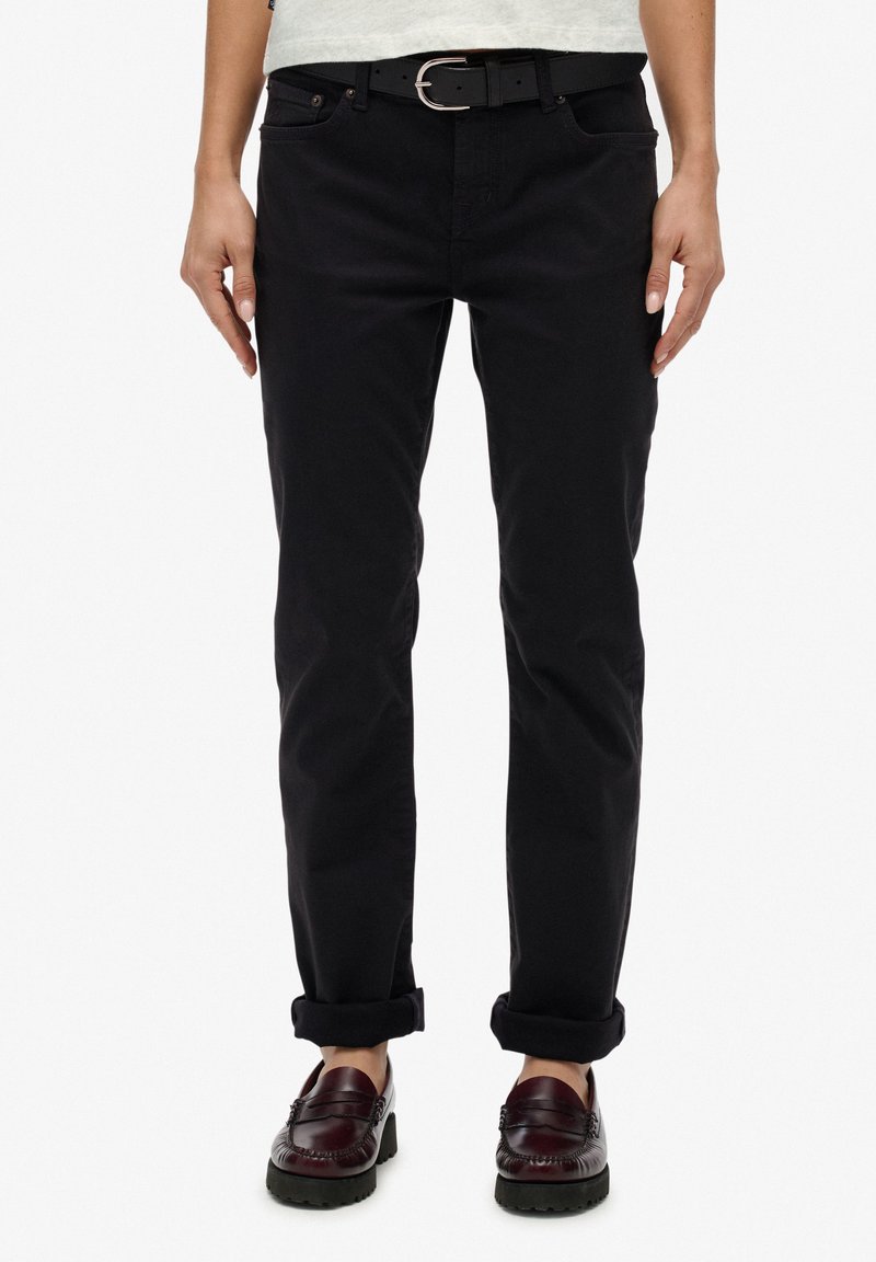 Pantalones ajustados negros de algodón, con cinco bolsillos y puños enrollados. Combinados con un cinturón negro y mocasines burdeos oscuros.