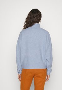 Ljusblå oversize-tröja med hög krage och ribbad fåll, ihopparad med orange ribbade byxor. Mjuk textur, avslappnad passform.