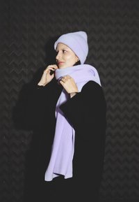 Berretto e sciarpa lavorati a maglia color lilla abbinati a un cappotto nero. La sciarpa è avvolta attorno al collo con una texture a costine.