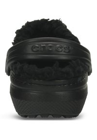 Schwarze Crocs mit einem fuzzy Innenfutter, ausgestattet mit einer strukturierten Gummisohle und einem breiten Riemen. Der Markenname "CROCS" ist auf dem Riemen eingeprägt.